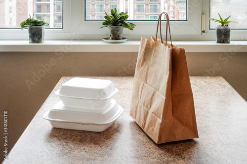 Two white styrofoam food containers and a paper bag on the kitchen table. Food home delivery concept