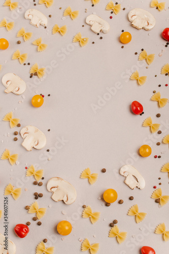 Uncooked pasta, tomatoes, mushroom slices and spices on a beige background, top view, close-up. Cooking, fettuccine, yellow and red cherries.