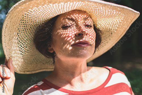 Close-up photo of senior charming brunette woman in hat blinks one eye and looking at camera