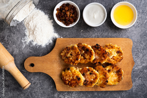 Homemade cheesecakes on a board with honey, raisins, sour cream on a stone background. Healthy food. Top view.