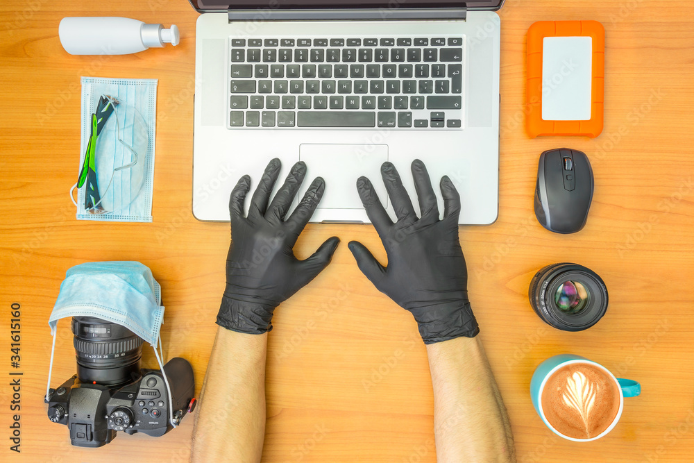 Male hands with black gloves working on laptop. Medical protection equipment, mask, sanitizer, glasses.