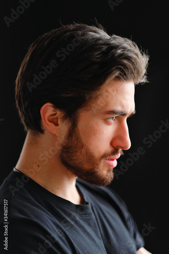 Close-up portrait of a young stylish man with a beard and dark hair in a black T-shirt 