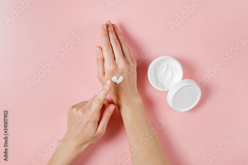 Revitalizing hand cream for healing and recovery after excessive use of soap and disinfectants. Young woman applying moisturizing lotion. Copy space, close up, pink background, flat lay, top view.