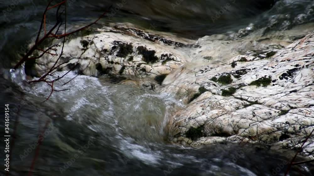 Close on a granite rock midstream of a fast moving wild and scenic river creating light and dark river water patterns and flow. Close on a granite rock midstream of a fast moving wild and scenic river creating light and dark river water patterns and flow.