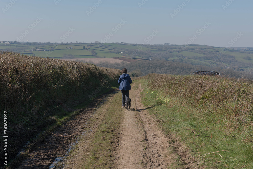 Adult Female Dog Walker with her Black Schnoodle Dog Walking Along a Farm Dirt Track in Rural Devon, England, UK