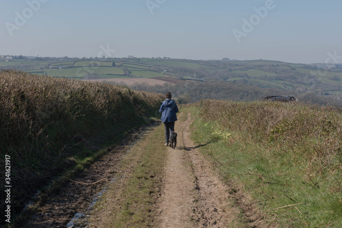 Adult Female Dog Walker with her Black Schnoodle Dog Walking Along a Farm Dirt Track in Rural Devon, England, UK © Peter