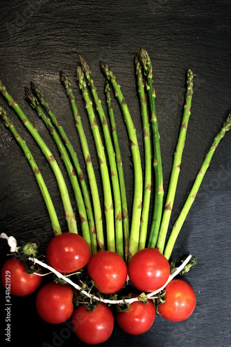 vegetables (green asparagus and tomatoes) on a black board top view