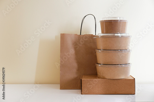 Bunch of blank disposable containers for takeout food stacked with paper bags and boxes with copy space for brand's logo. Close up shot of eco friendly to go carton bowls on table.