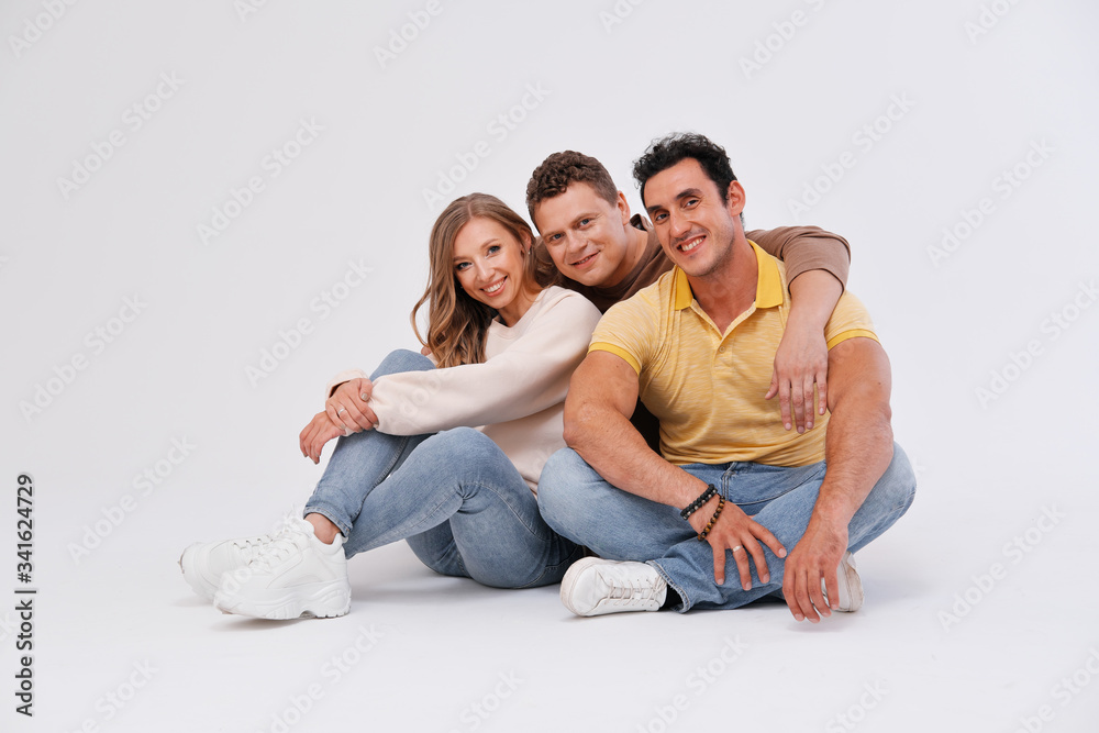 Three friends are sitting on the floor, hugging and smiling on a light background. Three friends are sitting on the floor, hugging and smiling on a light background.