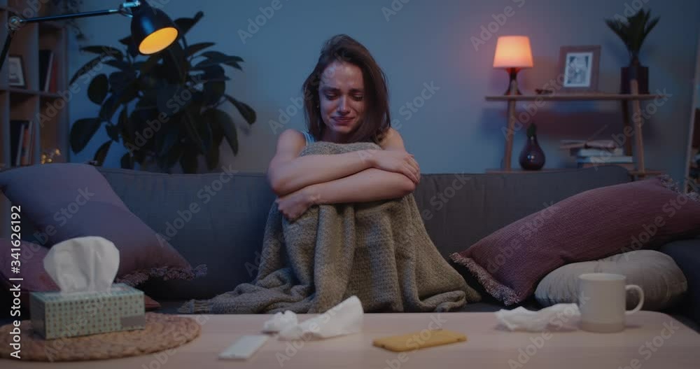 Front view of sad girl sitting alone on sofa in room and hugging her ...
