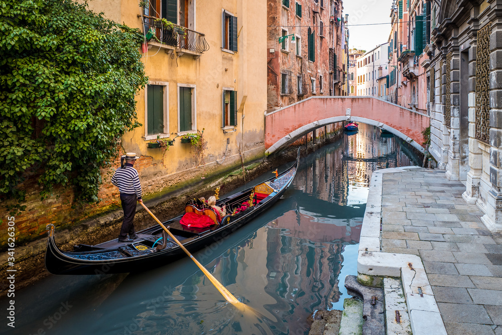 Gondola with tourists sails on old canal under medieval Bridge of Sighs, Venice, Italy. Famous historical landmark of Venice. Romantic water trip across Venice. 