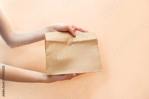 Close-up of cropped hands holding a brown transparent empty black Kraft paper takeaway food bag isolated on a yellow background Layout of the packaging template. The concept of service delivery.