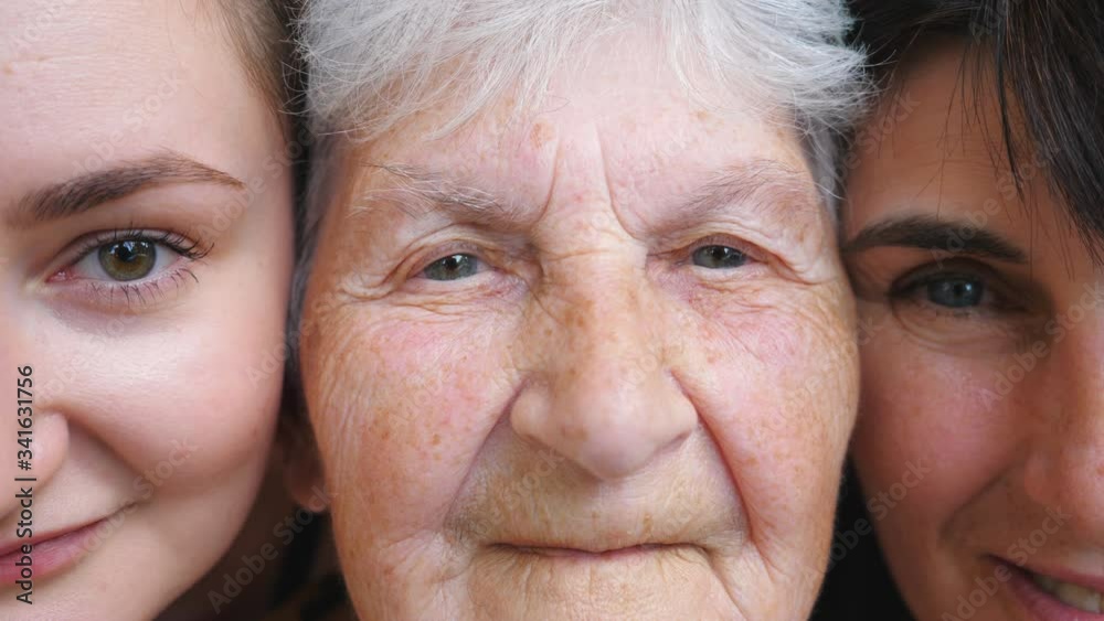 Portrait of elderly woman with her daughter and granddaughter looking into camera and smiling together. Happy ladies showing joyful emotions on faces. Positive facial expression of women. Close up Portrait of elderly woman with her daughter and granddaughter looking into camera and smiling together. Happy ladies showing joyful emotions on faces. Positive facial expression of women. Close up
