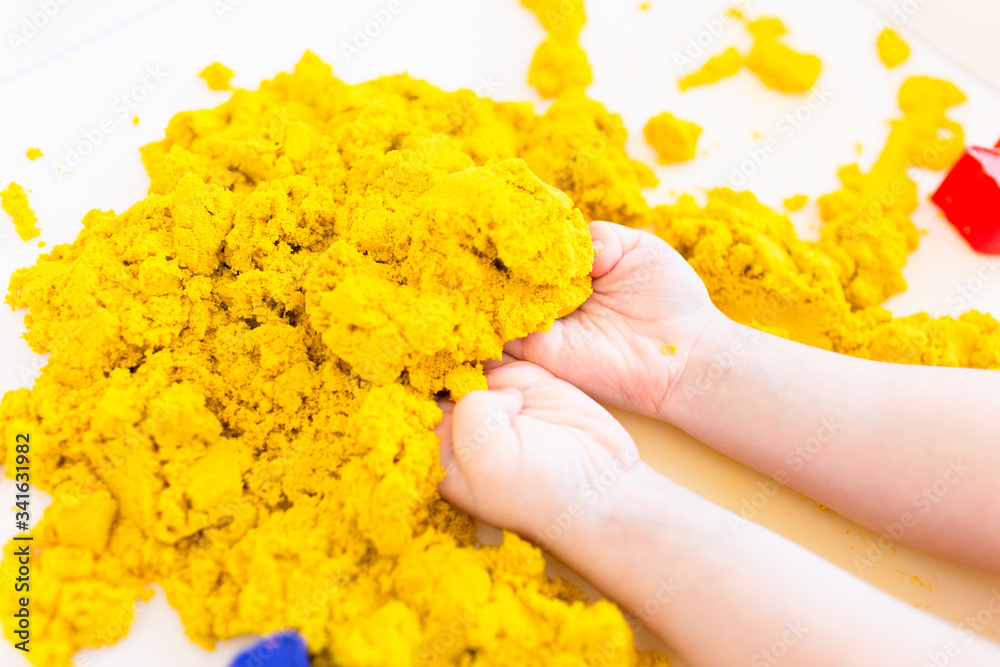 Yellow magic sand in a kids hands on a white background close up. Early sensory education. Preparing for School. Development - obrazy, fototapety, plakaty 