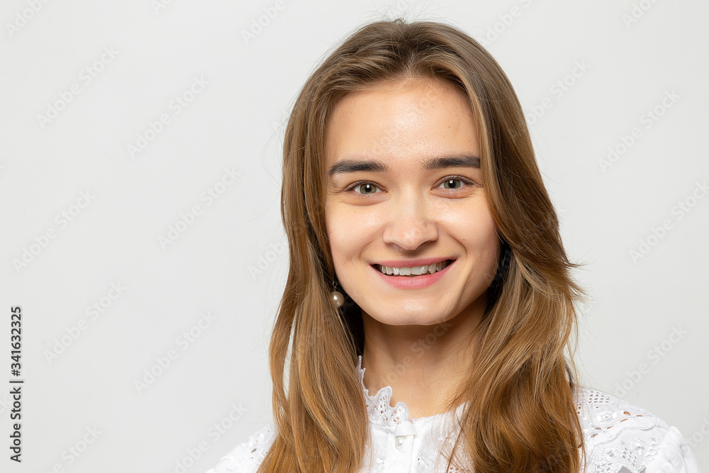 Closeup portrait of a beautiful young girl with dark hair in a studio on a white-gray background.