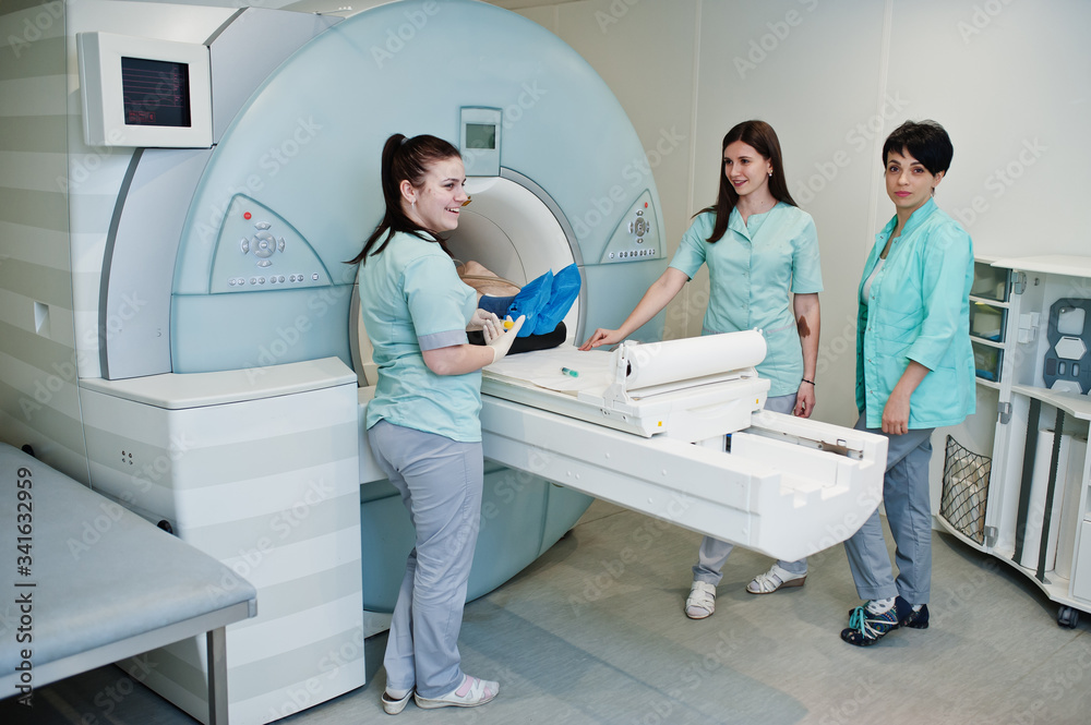 Three female doctors near magnetic resonance imaging machine with patient inside. Three female doctors near magnetic resonance imaging machine with patient inside.