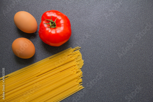 Tomato, eggs and pasta on a gray table.