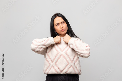 Portrait Young beautiful brunette in a white warm winter sweater holding hands in fists, aggressive facial expression.