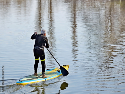 An elderly man swims in the water on a sports tourist inflatable spray with a paddle. Activity of people in old age. Modern water sports. Surfing with a paddle. Active recreation on the water