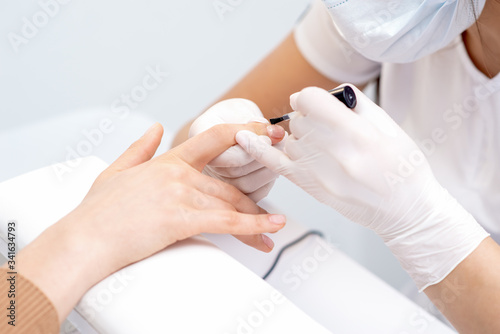 Manicure master hands covering clear varnish to female nail. Care nail fingers of hands.