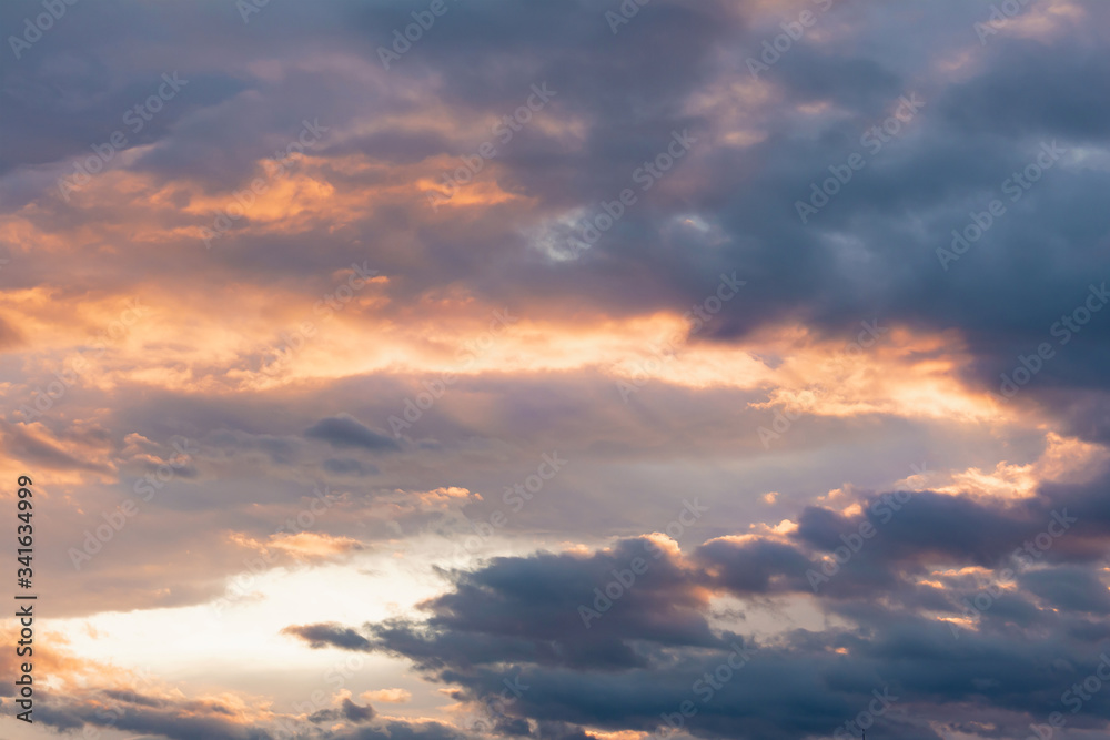 The dark sky at sunset through the clouds which break through the sun's rays forming clouds of orange and pink. Concept landscape, abstraction.