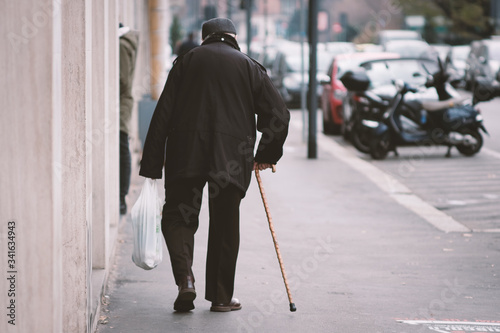 Vecchio con il bastone che cammina sul marciapiede in città a Milano