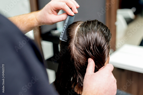 Hairdresser's hands are combing wet hair of woman in hair salon.