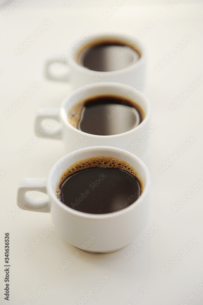 Black coffee in white cups one after another on white background Black coffee in white cups one after another on white background