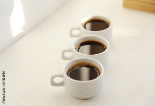 Black coffee in white cups one after another on white background