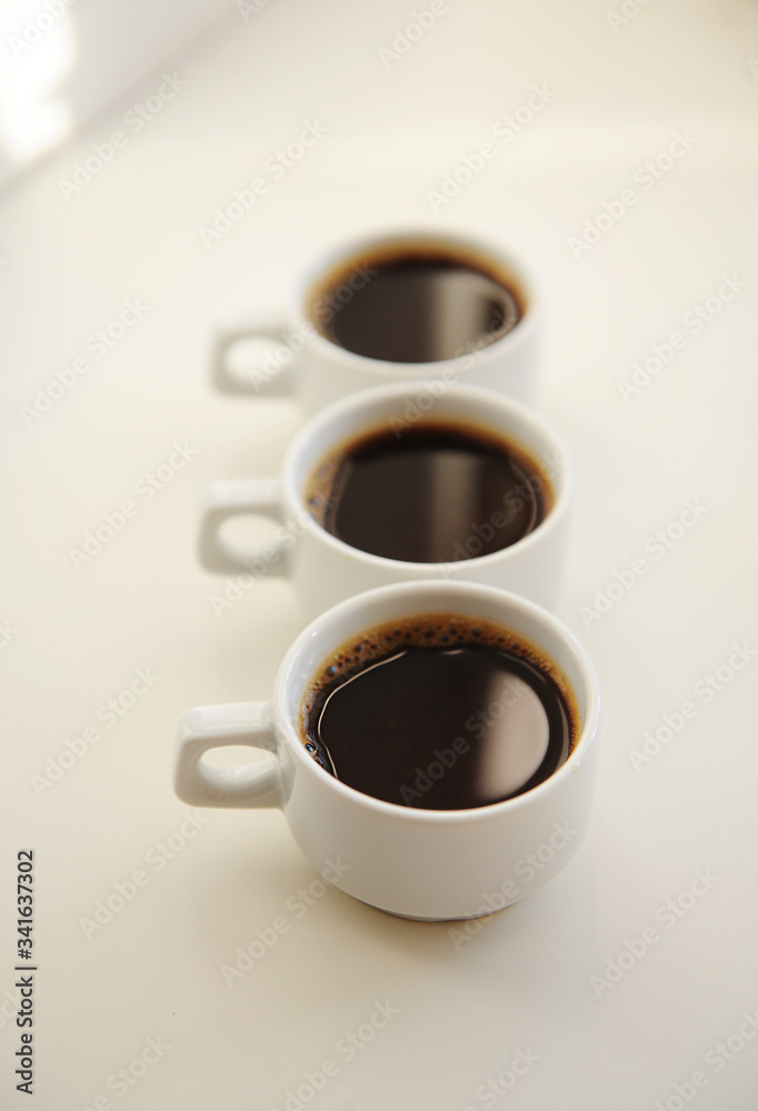 Black coffee in white cups one after another on white background Black coffee in white cups one after another on white background