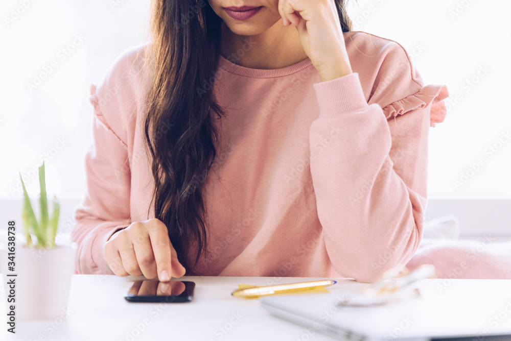Young woman using mobile phone while working at home with laptop. Young woman using mobile phone while working at home with laptop.