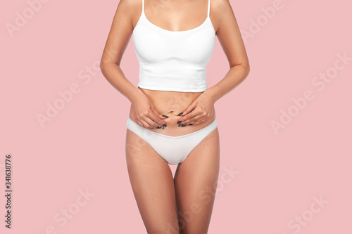 Young, healthy and beautiful blonde woman in white lingerie. Sport, fitness, diet, weight loss and healthcare concept. Slim female belly, girl holding her skin for cellulite check.