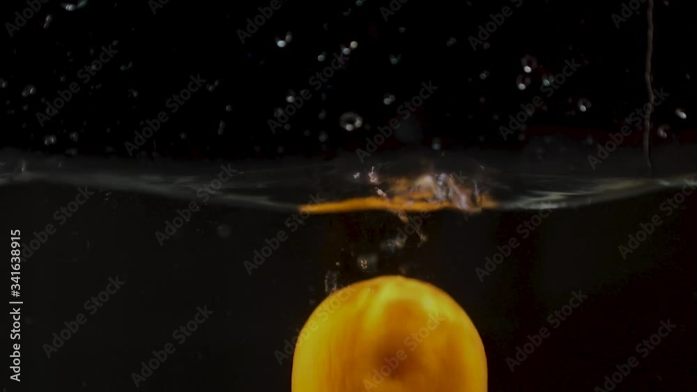 A lemon and a slice of lemon fall into the water with a splash. Slow motion.