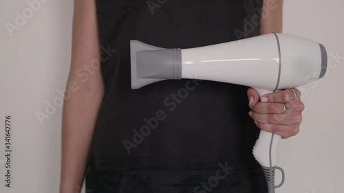 Detail shot of hairdresser woman's hands holding and demonstrating professional barber tools installing hair dryer nozzle with black apron background on hairstyling salon 