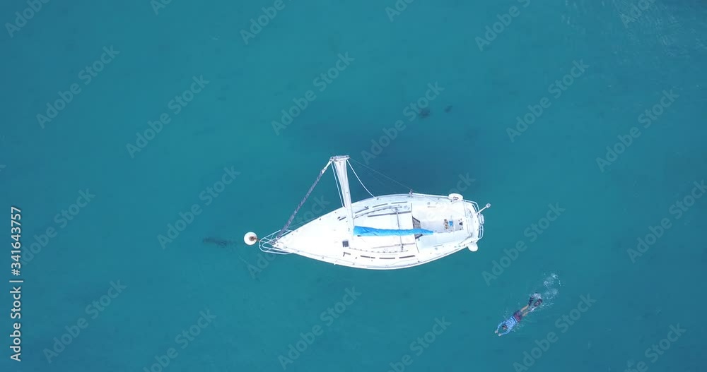 A person snorkels around a sailboat on a calm day in the ocean. A person snorkels around a sailboat on a calm day in the ocean.