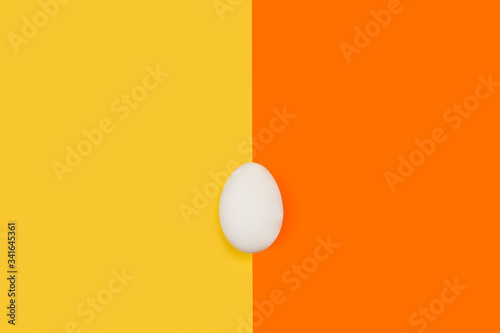 Fotografi Huevo blanco fresco y natural sobre fondo liso naranja y amarillo