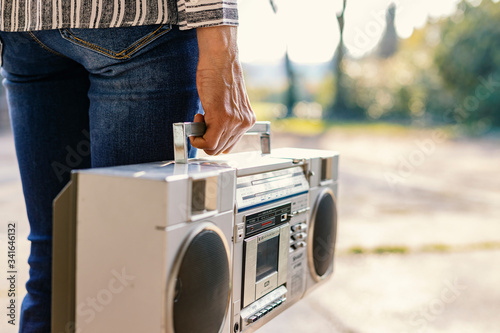 A woman holding a boombox. This retro style radio was very popular in the eighties, and people could carry it around.