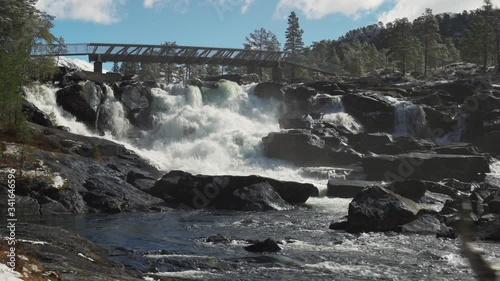 A beautiful view of the Likholefossen waterfall in Norway.  White-water gushing from under the bridge, powerful current of the mountain river. Water spray in the air. Stones are wet and glossy. photo