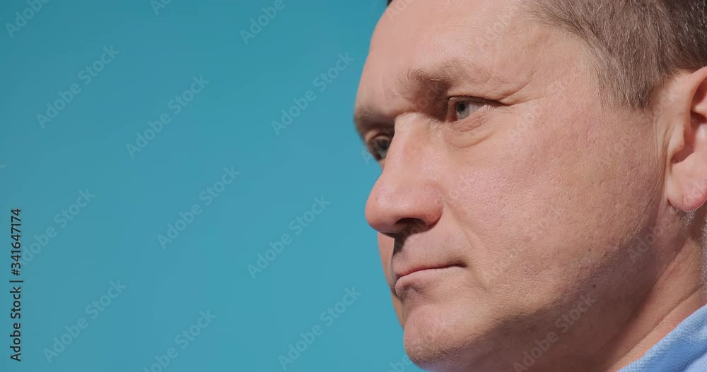 serious mature man touches eye and scratches eyebrow with fingers against blue wall slow motion extreme close view serious mature man touches eye and scratches eyebrow with fingers against blue wall slow motion extreme close view