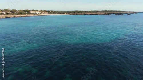 Flying Over The Son Xoriguer Beach With Turquoise Blue Water And Green Landscape On The Ground In Ciutadella Menorca, Spain.- aerial shot photo