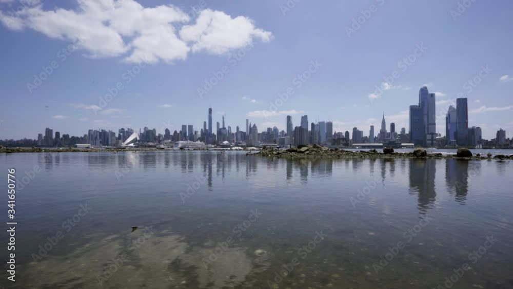 NYC skyline reflecting on shallow Hudson River as camera moves along water with blue sky white clouds NYC skyline reflecting on shallow Hudson River as camera moves along water with blue sky white clouds