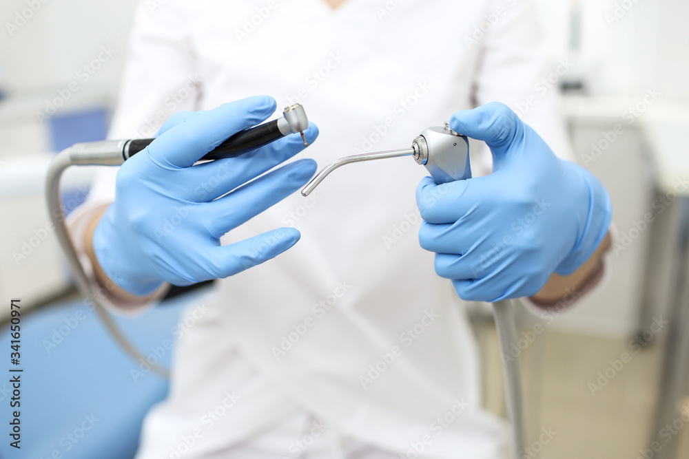 Closeup of dental instruments in hands of doctor in white mask. Selective focus Closeup of dental instruments in hands of doctor in white mask. Selective focus