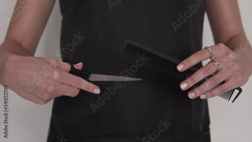 Detail zoom in shot of hairdresser woman's hands holding and demonstrating professional barber tools comb and scissors with black apron background on hairstyling salon 