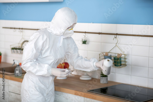 Woman in white workwear and gloves disinfecting the kitchen photo