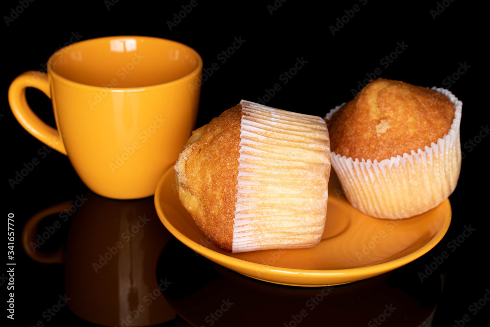 Group of two whole small baked muffin on plate with yellow cup isolated on black glass Group of two whole small baked muffin on plate with yellow cup isolated on black glass