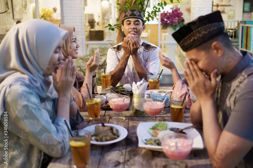 muslim family praying before eating their food. breaking the fast or iftar dinner