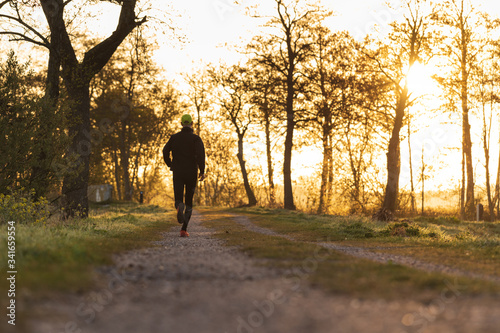 A man running during a spring sunrise in the countryside, with the sun in the background. © sanderstock