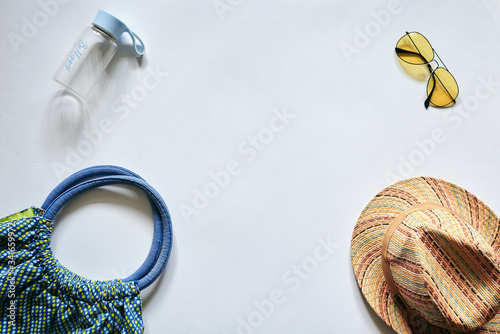 Flat lay picture of summer vacation beach accessories, isolated on white background. Straw hat, yellow sunglasses, blue beach bag and small bottle of water. Tropical vacation planning.