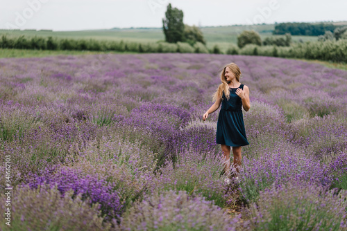 Beautiful woman walk and look on the lavender field on sunset in France. Beautiful girl in dress stand on purple the lavender field. Soft focus. Enjoy on the floral glade, summer nature.