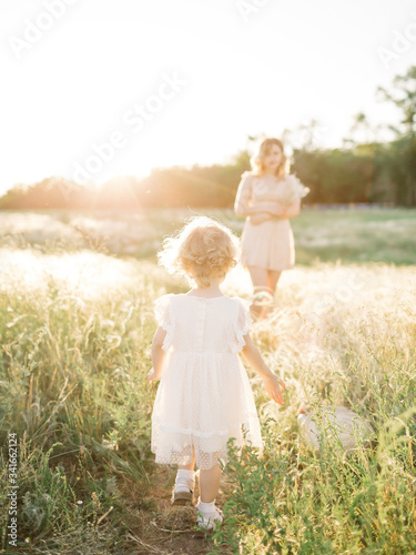 Young mother and baby girl in sunlight at sunset on nature outdoors. Mother and child in meadow in early summer. Photo of natural parenting, dreams, family values, sustainable lifestyle.